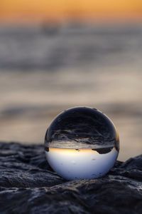 Close-up of ice cream on rock at beach against sky during sunset