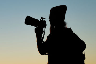 Silhouette woman photographing against clear sky during sunset