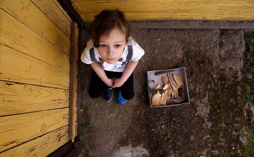 Portrait of girl sitting on wood against wall