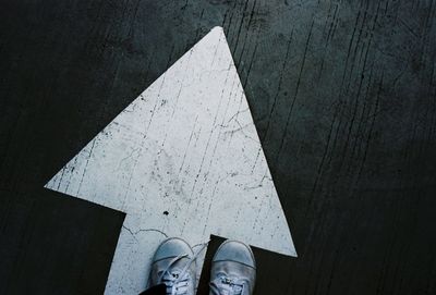 Low section of person wearing shoes standing on arrow symbol at road 