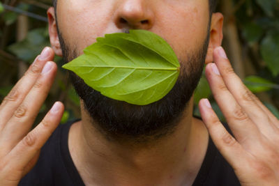 Midsection of man with leaf on mouth touching ears