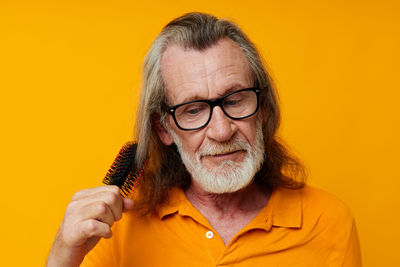 Senior man combing hair against yellow background