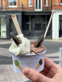 Womans hand is holding cup with two ice cream scoops. vanilla and hazelnut ice cream with chocolate