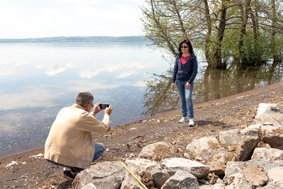 Man photographing while standing on rock by lake