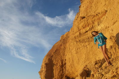 Low angle view of woman standing on rock against sky