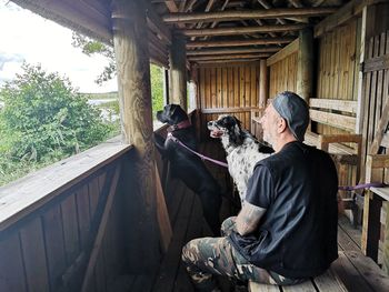 Man sitting with dogs at balcony in log cabin 