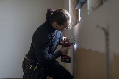 Side view of woman photographing against wall at home