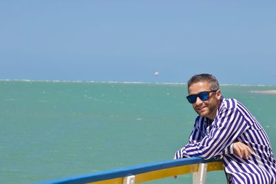 Man wearing sunglasses standing by sea against clear sky