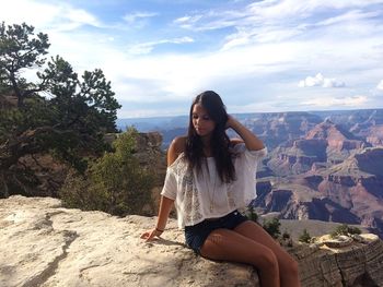 Woman relaxing on rock formation against cloudy sky at grand canyon