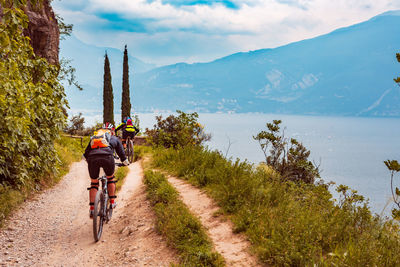 People riding bicycle on dirt road against sky