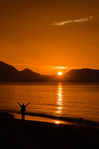 Silhouette person in sea against sky during sunset