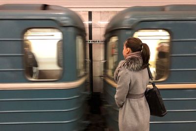 Side view of mid adult woman in warm clothing standing at railroad station platform