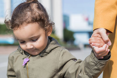 Close-up of cute daughter holding mother hand in city