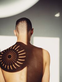 Rear view of shirtless man standing against wall