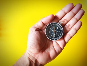 Close-up of person hand holding ring over yellow background