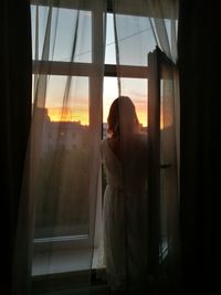 Woman looking through window at home