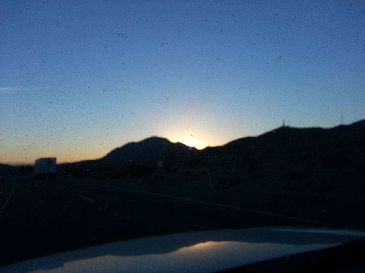 transportation, mountain, clear sky, landscape, scenics, road, beauty in nature, copy space, tranquil scene, sunset, sky, silhouette, nature, tranquility, mode of transport, car, mountain range, road marking, no people, blue