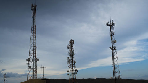 Low angle view of communication towers on field against cloudy sky