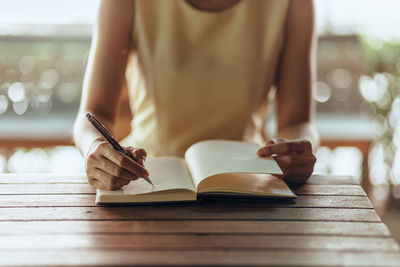 Midsection of woman writing in book on table