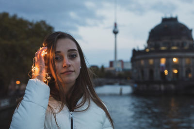 Portrait of young woman holding illuminated lights with fernsehturm in background