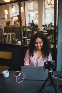 Confident young female influencer using laptop while vlogging at creative office