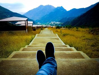 Low section of person on road by mountains against sky