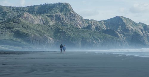 Distant view of friends walking at beach against mountains
