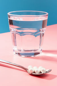 Glass of water and collagen capsules on a pink and blue background.