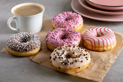 Several donuts lie on craft parchment paper. cup of coffee and pink plates stands next to donuts. 