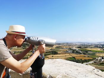 Side view of mature man looking through telescope against sky during sunny day