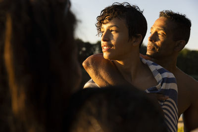 Man with arm around son looking away during sunset