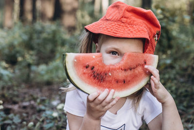 Portrait of cute girl holding watermelon standing in forest