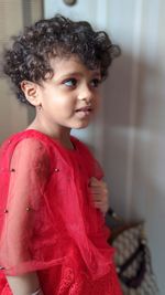 Close-up of smiling girl looking away standing by wall at home