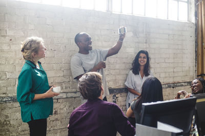 Cheerful male it expert showing smart phone to professionals at workplace