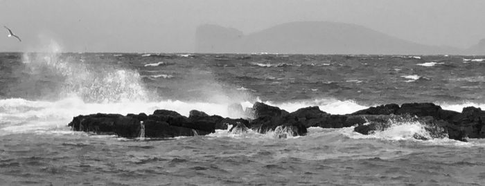 Scenic view of sea waves splashing on shore against sky