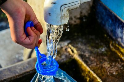 Cropped hand of woman filling bottle from faucet