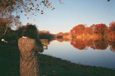 Rear view of woman looking at trees reflection in lake against sky