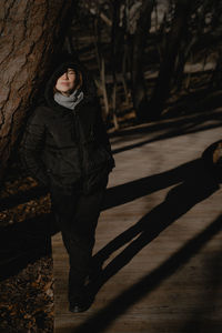 A woman stands with her eyes closed, leaning against a tree, enjoying the bright sunlight 