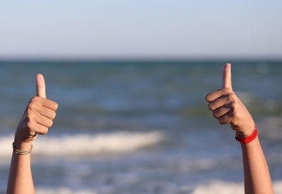 Cropped hands showing thumbs up at sea against sky