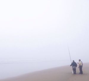 Fishermen standing with fishing rod at beach in foggy weather