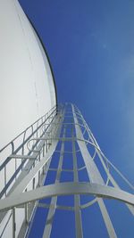 Directly below view of metallic ladder on white silo against blue sky