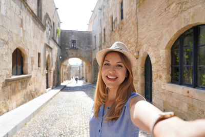 Happy smiling traveler girl taking selfie in the street of the knights of rhodes city, greece. 