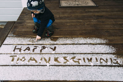 High angle view of baby boy writing thanksgiving text with snow on floor