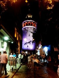 People on illuminated street amidst buildings in city at night