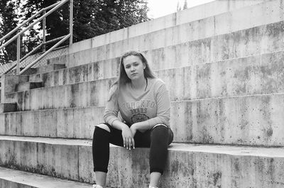 Portrait of young woman sitting on staircase against wall