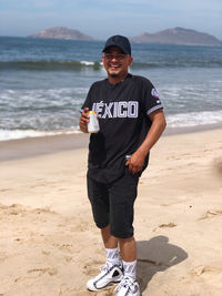Portrait of smiling man holding drink standing at beach