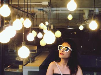 Portrait of woman wearing sunglasses against illuminated lights