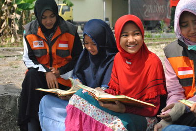 Women in hijab reading books while sitting outdoors