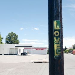 Love text on wooden post at street against sky