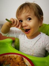 Portrait of baby girl eating food in high chair at home